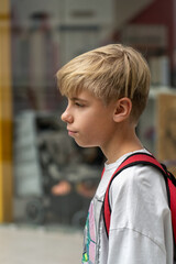 Fototapeta premium Teen boy with blonde hair and a backpack standing at shopping mall