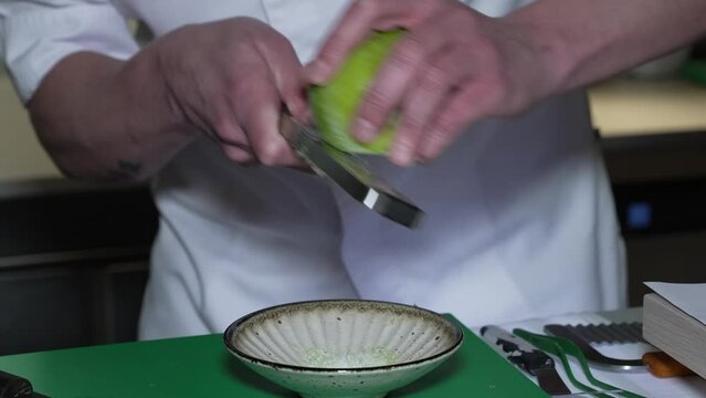 Las manos de un cocinero rallando una manzana verde para realizar un postre.