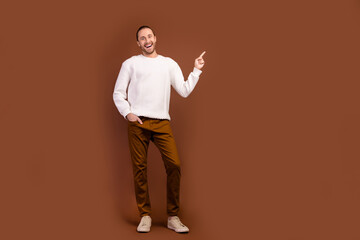 Fototapeta na wymiar Full length photo of cheerful impressed guy dressed white pullover pointing finger empty space isolated brown color background