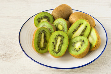 On a white plate on the table there is fresh kiwi fruit cut in half.