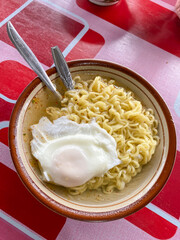 Delicious hot instant noodle soup topped with poached egg in brown ceramic bowls on a table. Concept for unhealthy junk food, Ultra processed food.