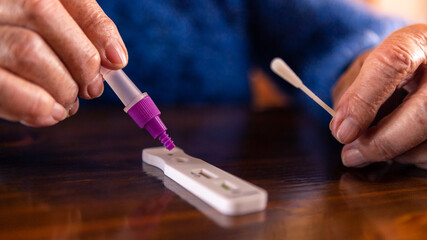 Close-up of caucasian grandma placing sample into buffer dropper for coronavirus