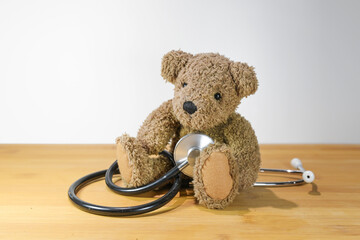 Little toddler teddy bear sitting on the table and playing with a stethoscope like a child, concept...