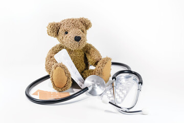 Teddy bear sitting with pills, plaster and stethoscope on a white background, health care for children and pediatrics, but also danger when playing with medicine, copy space