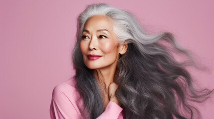 Smiling, elderly, gorgeous Asian woman with gray long hair and perfect skin, on a pink background, banner.