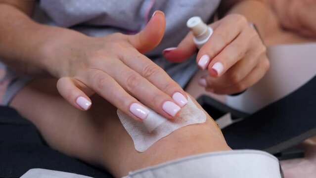 A wooman wearing sterile gloves sticks a medical patch on the postoperative stitches on the knee joint.