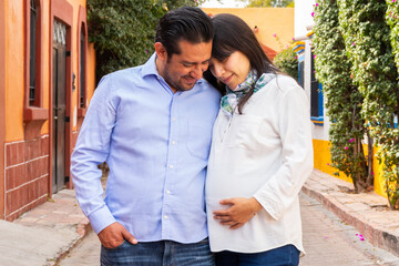 A couple shares a heartfelt moment on a quaint street in Tequisquiapan with the expectant mother cradling her seven month baby bump as they both look down affectionately