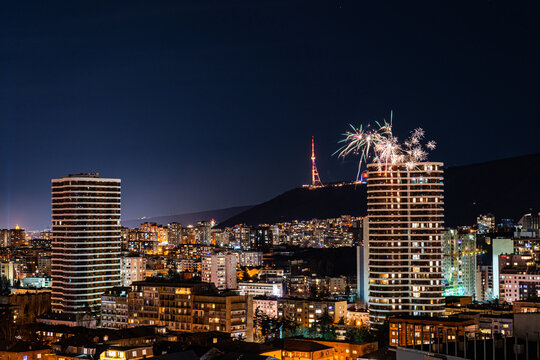 A vibrant display of fireworks bursting over the night sky of Tbilisi, lighting up the cityscape with various colors and patterns