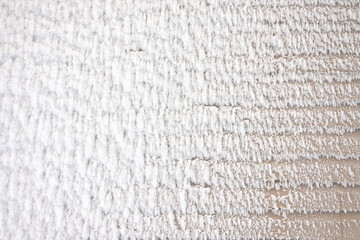 A fragment of the wall of a plastic clapboard house is partially covered with a thick layer of snowy frost. Background. Texture. Form.