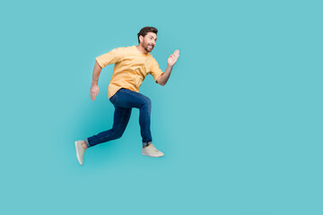 Fototapeta na wymiar Full body size photo of sportive man in yellow t shirt and denim jeans running air to his target isolated on aquamarine color background