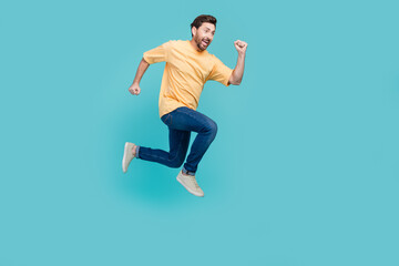 Fototapeta na wymiar Full body size photo of funky young brunet man in yellow t shirt and jeans jumping run to his dream isolated on blue color background
