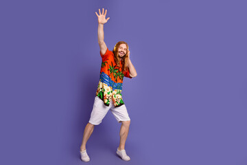 Fototapeta na wymiar Full size photo of cool man wear print shirt white shorts touch headphones raising hand up say hi isolated on purple color background