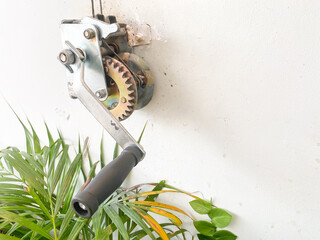 A hand winch mounted on a wall is used to open window curtains or the roof of a house. Winch...