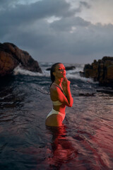 Attractive female enjoys nocturnal swim in sea under red illumination. Young woman in bikini experiences tranquil night dip amidst marine ambiance. Oceanic holiday, leisure travel for relax.