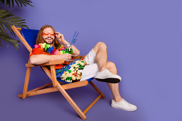 Obraz na płótnie Canvas Full size photo of funny positive man touch sunglass sit on armchair with cocktail at ocean beach isolated on purple color background