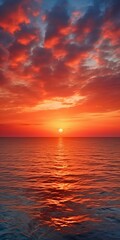 Fototapeta premium Sunrise over the ocean with vibrant orange and red clouds reflecting in the water, and with sun casting a golden path
