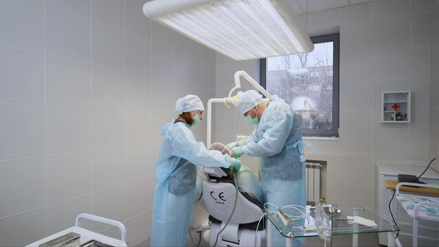 Dental implant surgery. Oral surgeon and assistant treating root canals in the modern dental clinic. Surgery operation performed by endodontist, nurse. Concentrated work of a stomatologist.