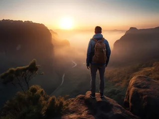 Fotobehang A traveler is looking towards the horizon as the sun rises over a beautiful scenic landscape. The traveler is standing on a cliff. © Aisyaqilumar