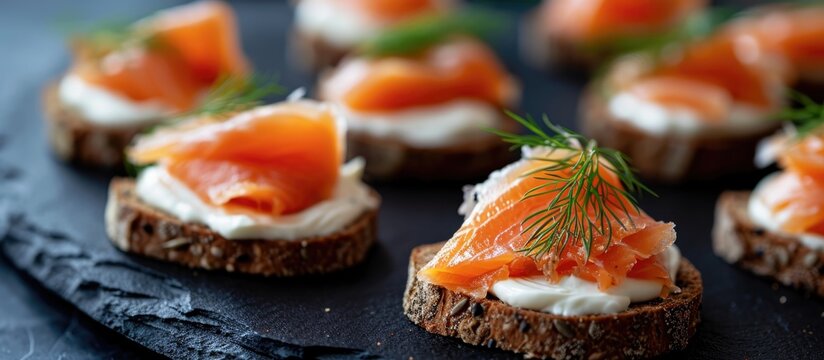Salmon canapes with cheese cream, dill, on brown bread, served on a black slate platter.