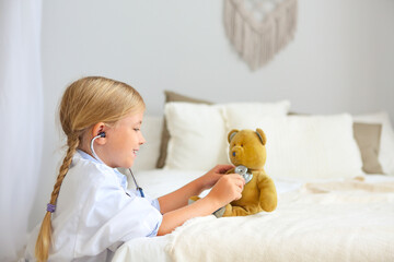 Little blond girl with stethoscope playing with teddy bear