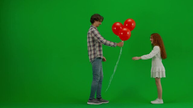 Little girl in white dress with red helium balloons on chroma key green screen isolated background young man brings girl bunch of balloons.