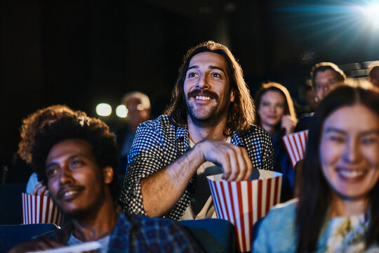 Smiling young man with popcorn watching movie in packed theater
