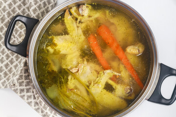 In a metal pot, chicken broth is simmered with pieces of chicken and vegetables.
