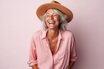 Portrait of a happy senior woman in hat laughing against pink background