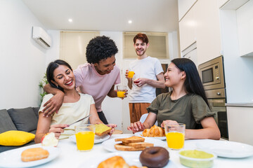A group of diverse friends share a laugh over breakfast with fresh juice and pastries in a bright, cozy kitchen.