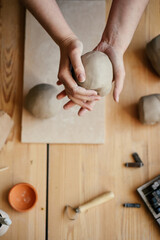 Ceramist Slapping a damp lump of clay with his hands. Round lump of raw white clay in hands Preparing for clay modeling in a workshop, top view