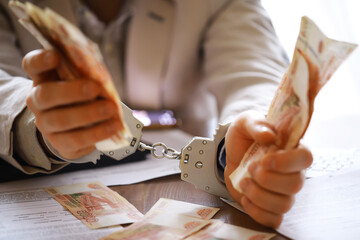 Fototapeta premium Hands in handcuffs behind, holding five thousand rubles. Concept of corruption