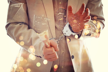 Double exposure of male hands locked in handcuffs with city landscape background, with cross...