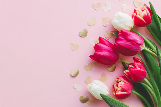 Stylish hearts and tulips on pink background flat lay. Happy Valentines day and happy mothers day. Valentine border gold hearts paper cutouts. Banner template, space for text