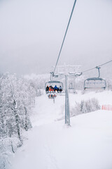 Fototapeta na wymiar Skiers in colorful ski suits ride through the snow-capped mountains on a chairlift