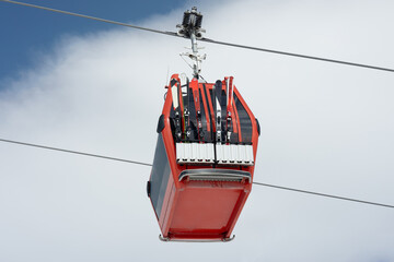 Close-up of cable car or ski lift cabin with alpine skis moving against the background of cloudy...