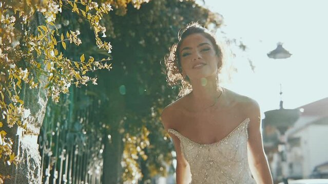 Pretty bride in long airy veil, elegant white dress runs away from camera on wedding day. Playful attractive woman running away turning, looking to viewer. Follow me concept