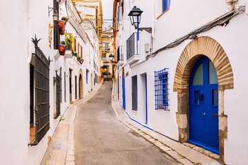 A charming narrow street lined with traditional white houses and blue accents in the coastal town of Sitges, near Barcelona.