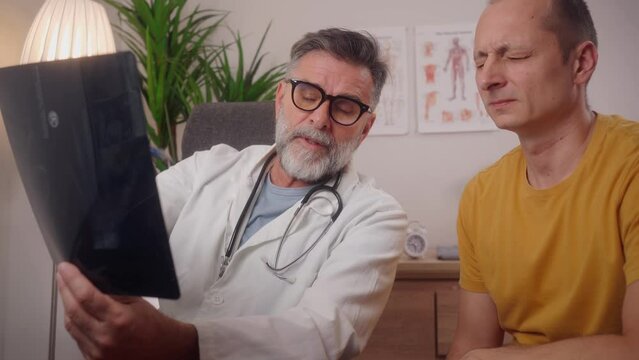 The doctor explains the severity of the hand injury on the x-ray, image while the patient is worried about his health. Anxious male patient at consultation with confident senior doctor.