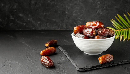 Juicy dates in a white bowl on a dark slate, against a textured backdrop. Ideal for Ramadan themes.