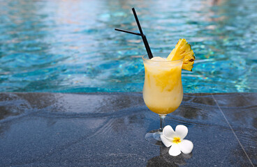 Glass of pinacolada cocktail standing on the swimming pool ledge