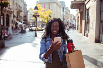 Smiling young woman using smartphone with shopping bags in city