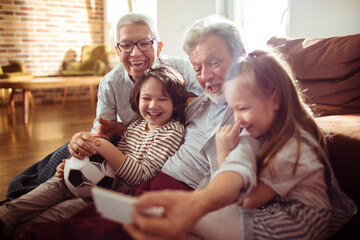 Happy grandparents taking selfie with grandchildren at home