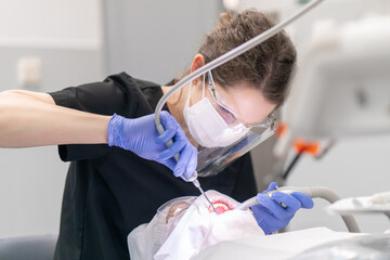 The dentist performs a procedure to clean the patient's teeth from plaque and tartar using an air...