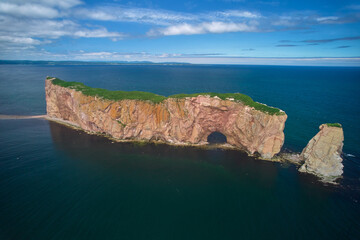 The beautiful colors, natural arch and shape of famous Perce Rock on the Gaspe Peninsula in Quebec Canada with it's red-pinkish colors from an aerial drone image