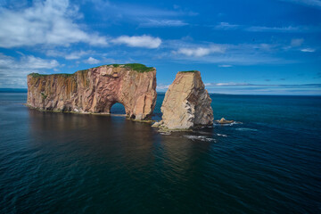 Fototapeta na wymiar The beautiful colors, natural arch and shape of famous Perce Rock on the Gaspe Peninsula in Quebec Canada with it's red-pinkish colors from an aerial drone image