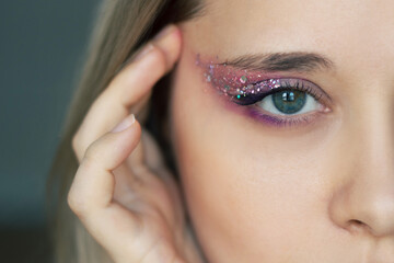Close up of a young caucasian blonde woman's green eye with purple and pink eye shadow and glitter...