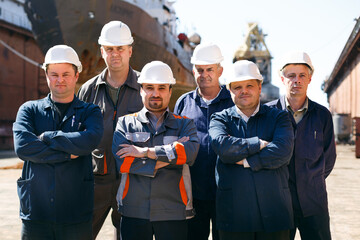 Shipyard workers at float dock wearing hard hats, stand arms-crossed. Male repair team ready for...