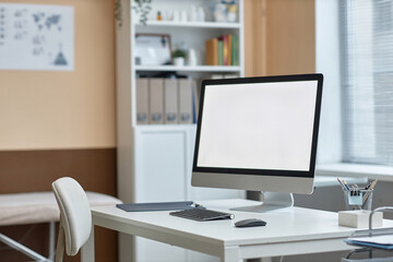 Medium shot of computer monitor with white copy space screen and stationery on table in doctors consulting room