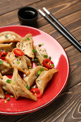Plate with tasty Chinese jiaozi, sesame and green onion on wooden background