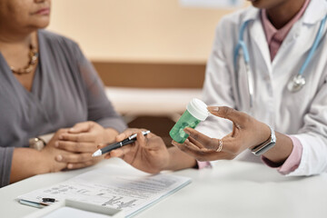 Fototapeta premium Close up shot of green plastic bottle with pills in hand of female doctor talking to patient during consultation in clinic